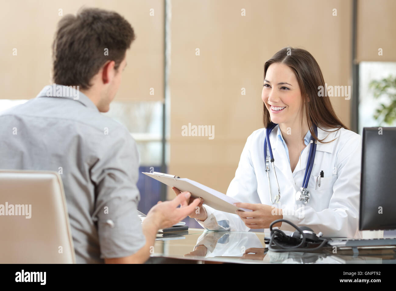 Felice medico femmina cappotto indossa frequentando il suo paziente in una consultazione mentre è in possesso di una storia medica Foto Stock