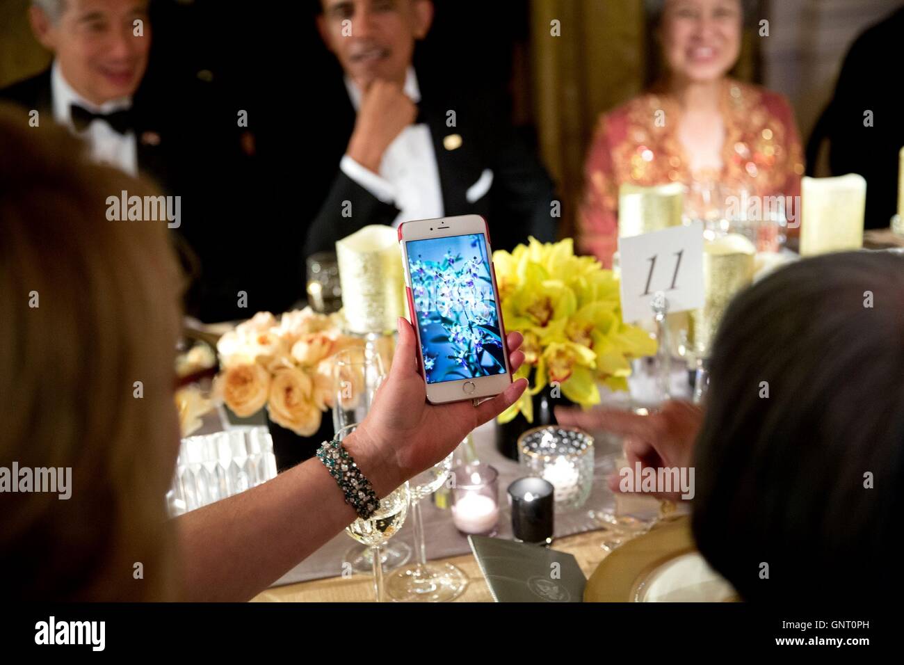 Il Presidente degli Stati Uniti Barack Obama sorrisi come membro per la cena gli ospiti visualizza una foto su un ibrido di orchidea telefono mobile che Singapore chiamato in onore di Obamas durante lo stato la cena nella Sala Est della Casa Bianca il 2 agosto 2016 a Washington, DC. Foto Stock