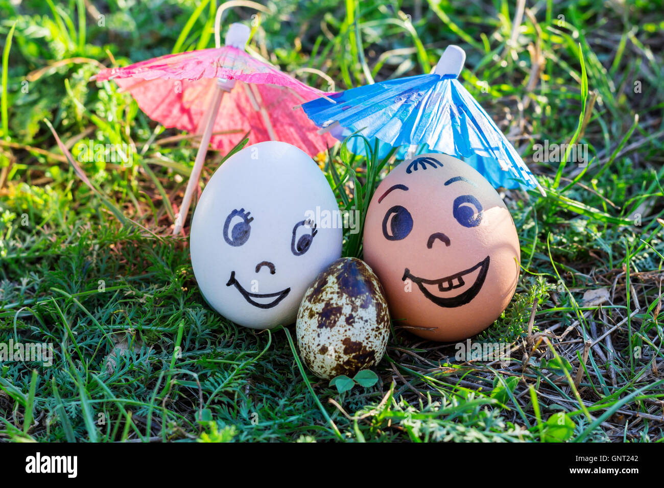 Uova divertente imitando sorridenti coppia mista bianca e colorata con i genitori versicolored baby sotto ombrellone Foto Stock