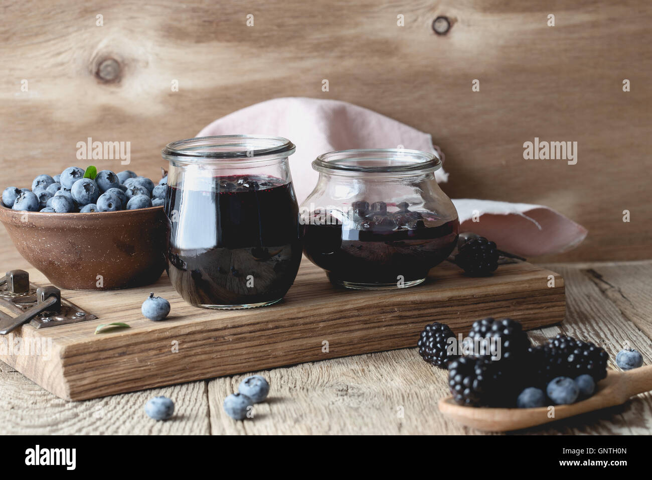 In casa i mirtilli e confettura di more in vasetti di vetro e di frutti di bosco freschi in legno tavolo rustico Foto Stock