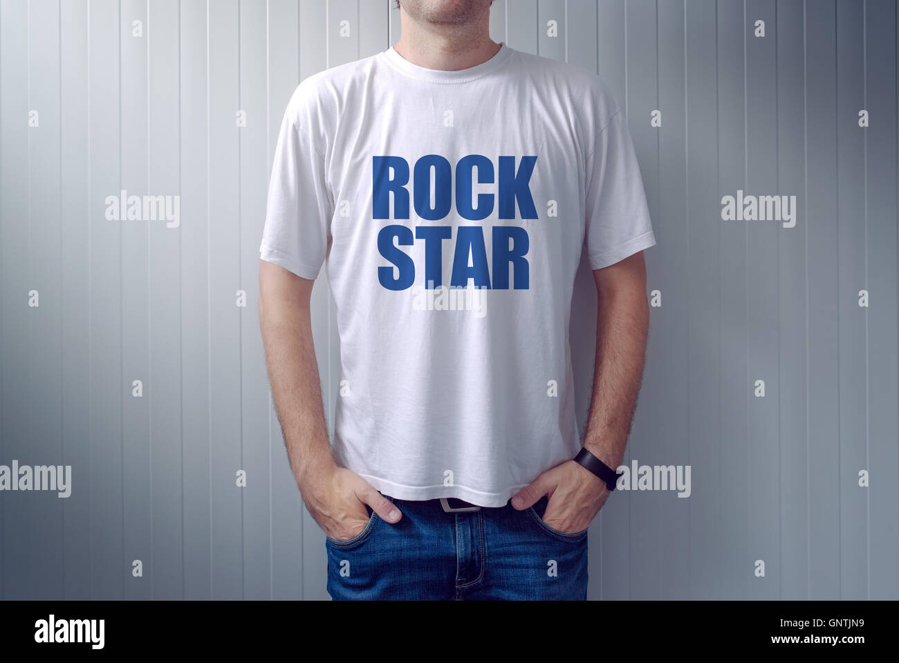 Casual maschio adulto che indossa la t-shirt con una rock star titolo, uomo in jeans appoggiata sulla parete Foto Stock