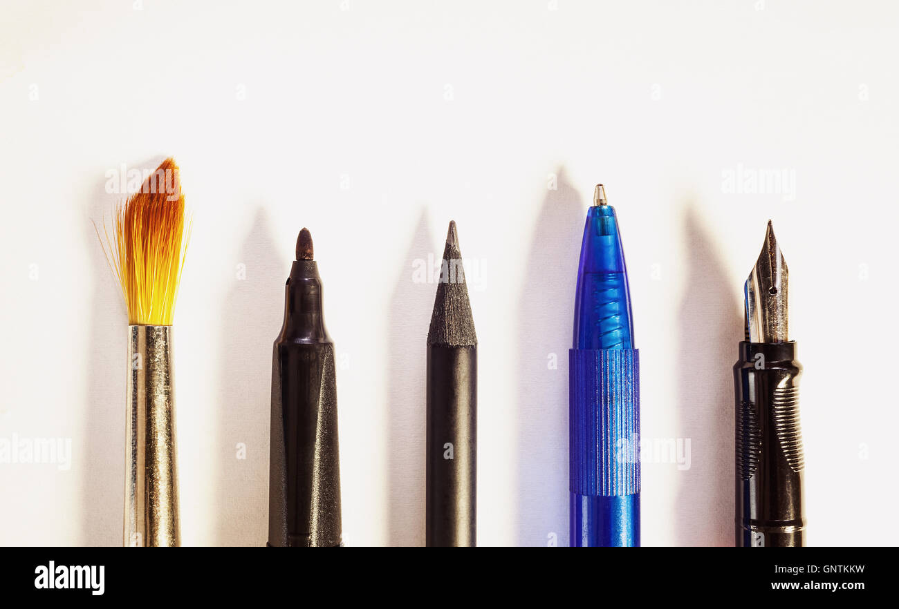 Vari strumenti per la scrittura o la pittura, composizione concettuale su carta bianca. Foto Stock