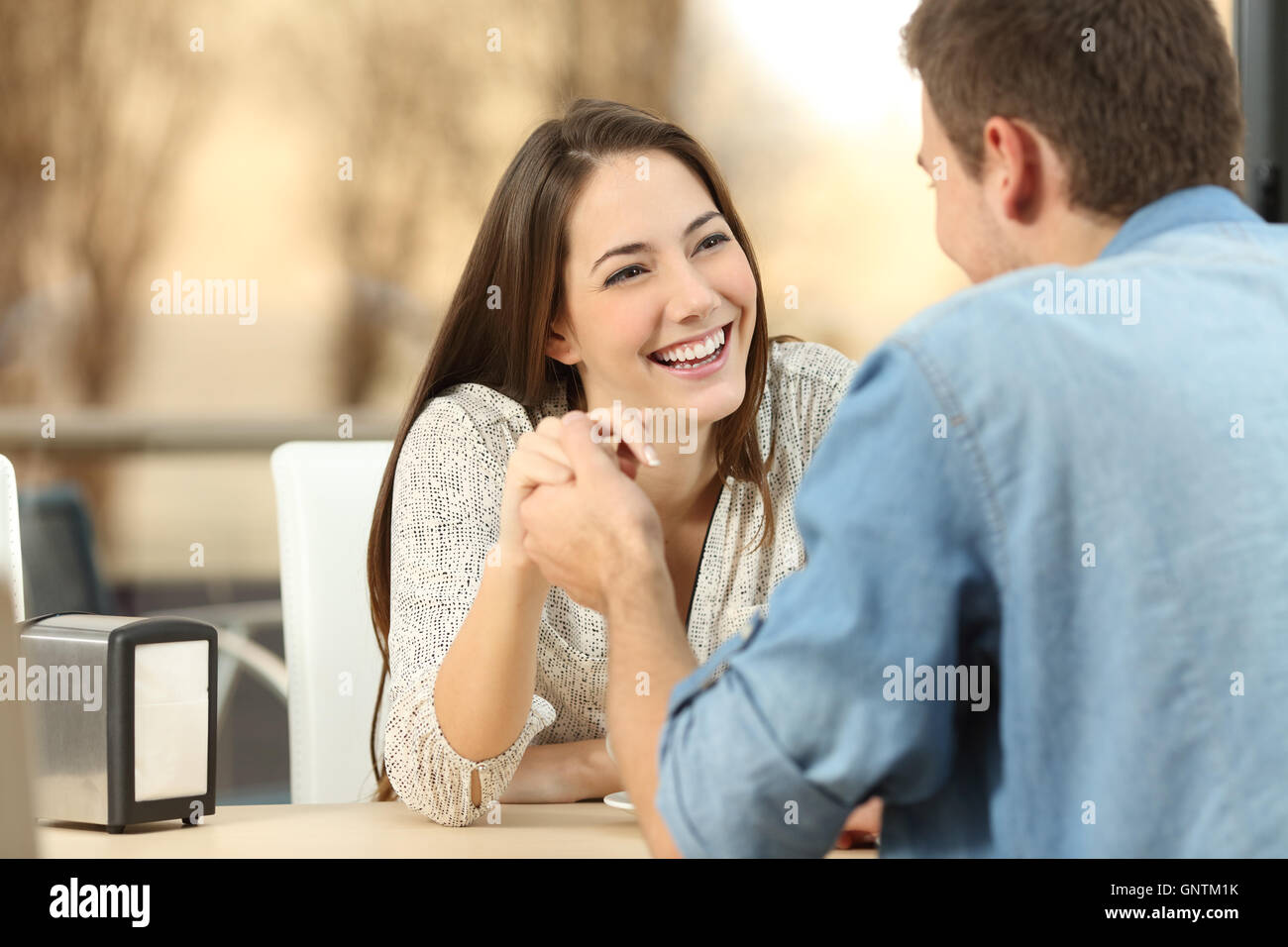 Felice coppia dating e flirtare e tenendo le mani insieme in un coffee shop con la luce del tramonto all'aperto in background Foto Stock