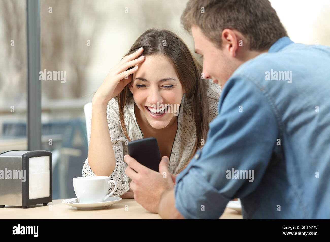 Allegro giovane ridere guardare i media in smart phone seduti in un caffè Foto Stock