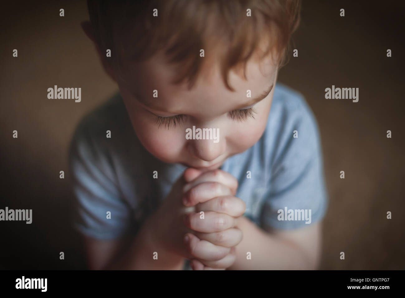 Un simpatico giovane ragazzo che prega con le mani incrociate. Foto Stock