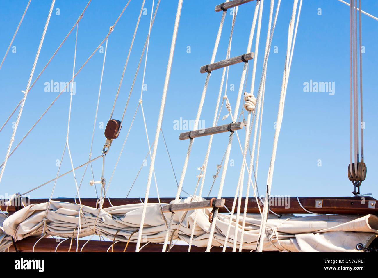 Dettaglio di una vecchia barca a vela vela avvolto, braccio, armamento e la scaletta di corda contro il cielo blu Foto Stock