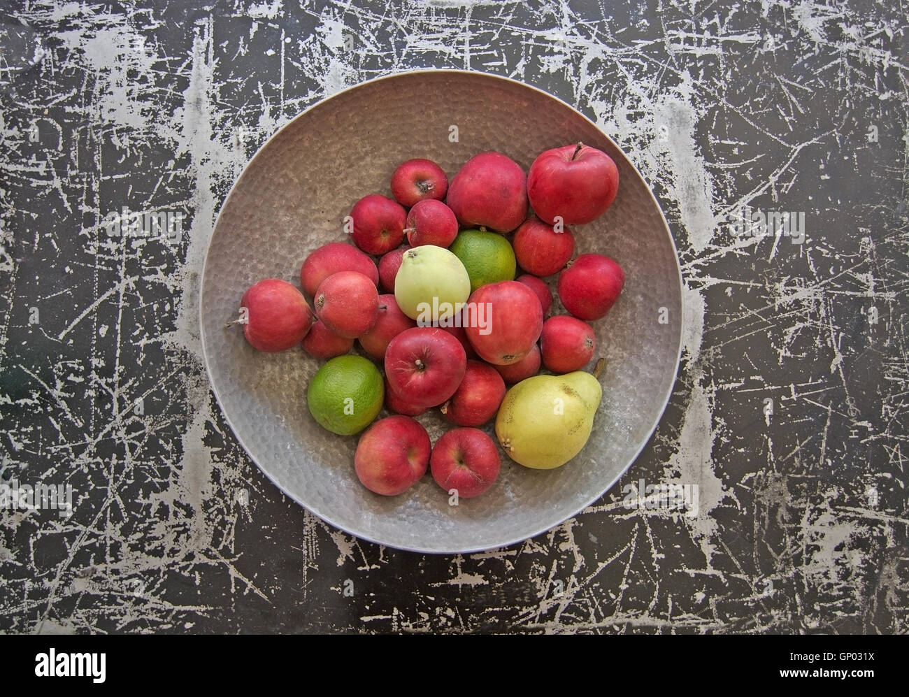 Colore argento ciotola di metallo con le mele rosse, una pera e la calce e la frutta in nero e in color argento di superficie metallica. Foto Stock