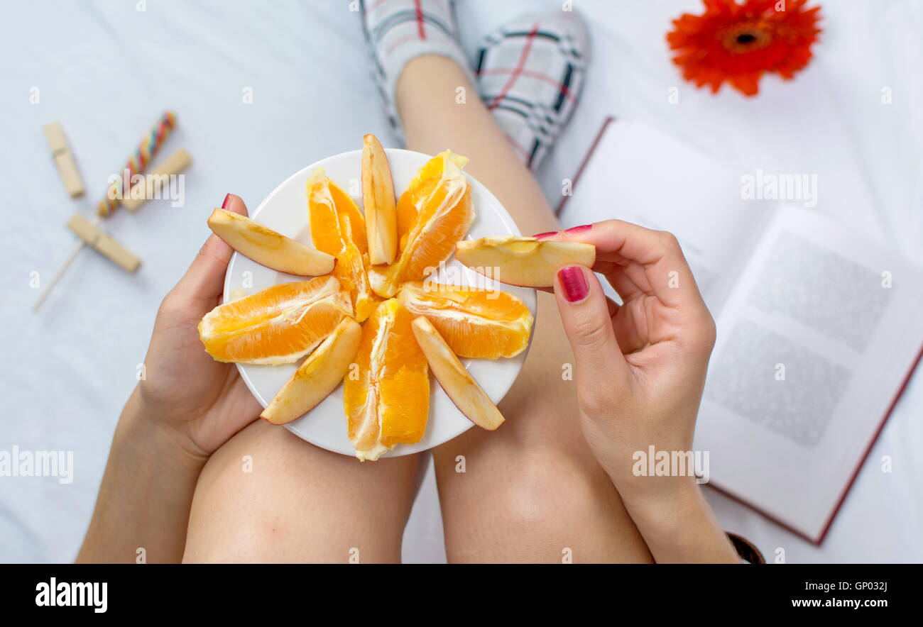 Donna di mangiare fresco frutta arancione nel letto Foto Stock