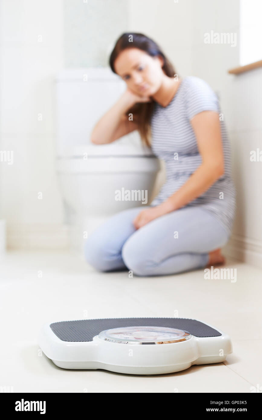 Infelice ragazza seduta sul pavimento Guardando bilancia da bagno Foto Stock
