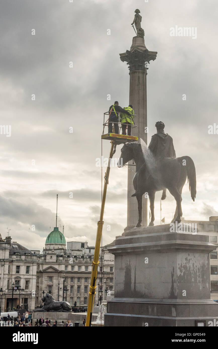 Operai pulizia della statua del re George IV statua su un nuvoloso pomeriggio. Lord Horatio Nelson può essere visto sulla cima di una colonna in background. Foto Stock
