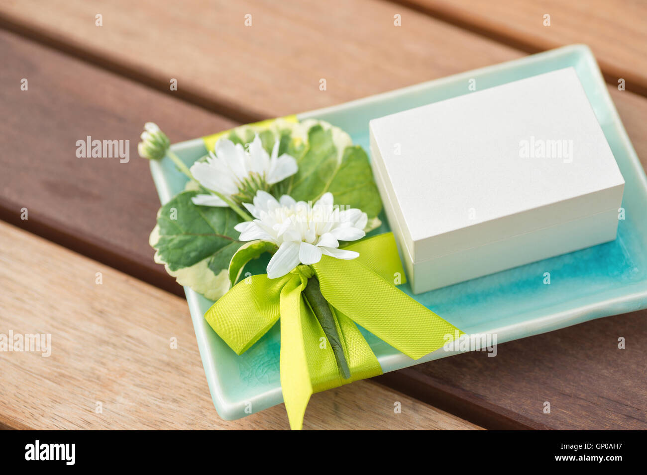 Una piccola casella bianca su decorate turchese Vassoio in ceramica con fiori di colore bianco e nastro verde Foto Stock