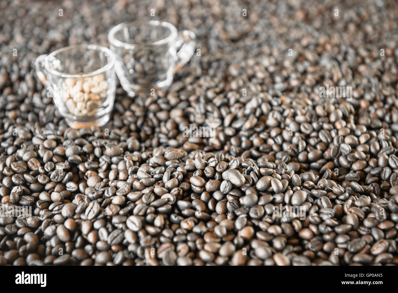 Chicchi di caffè tostati con sfocata 2 tazzine di caffè sul fondo. Foto Stock