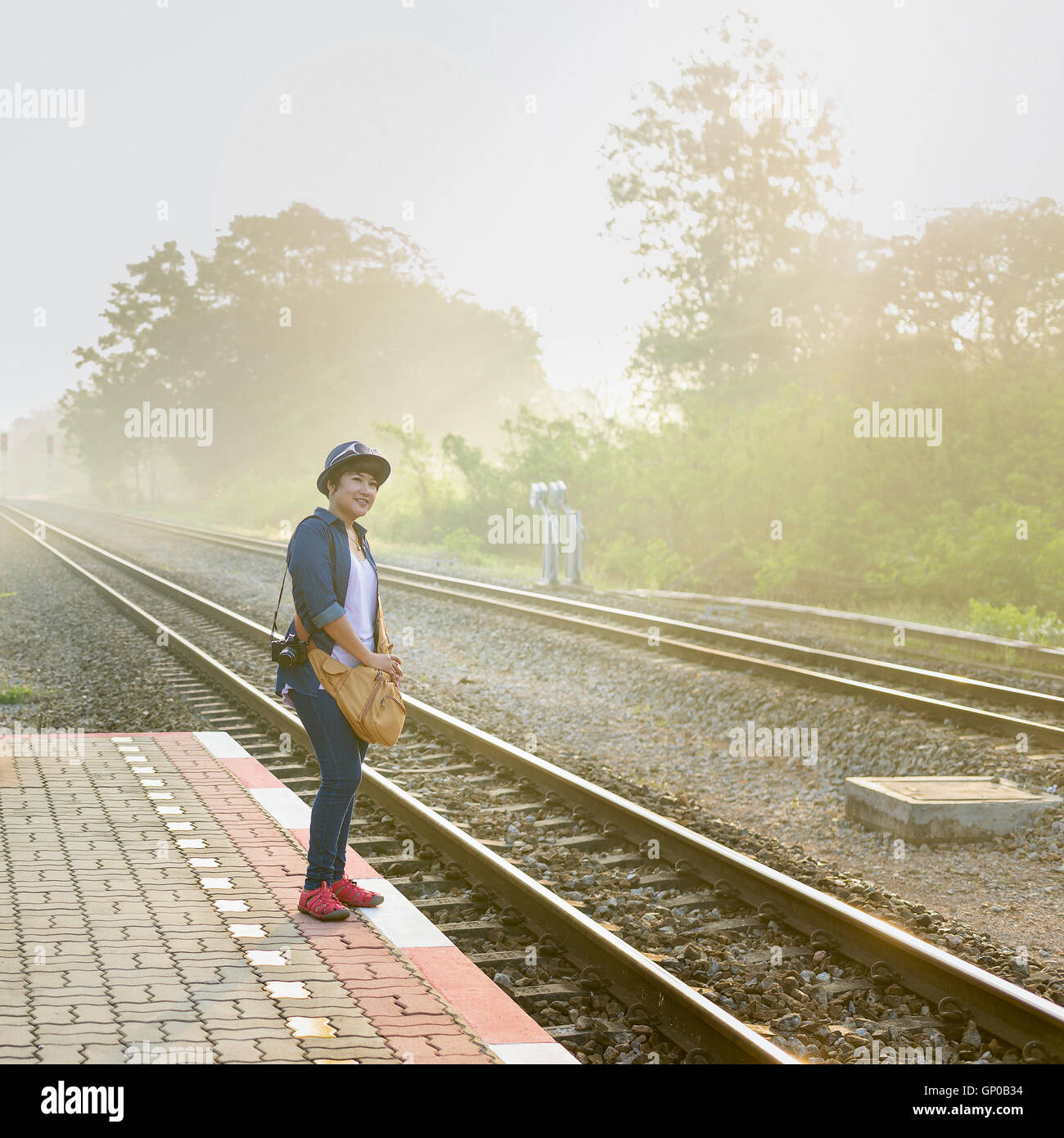 In una nebbiosa giornata di sole un donne asiatiche i viaggiatori in attesa di un treno sulla piattaforma a livello locale stazione ferroviaria. Foto Stock