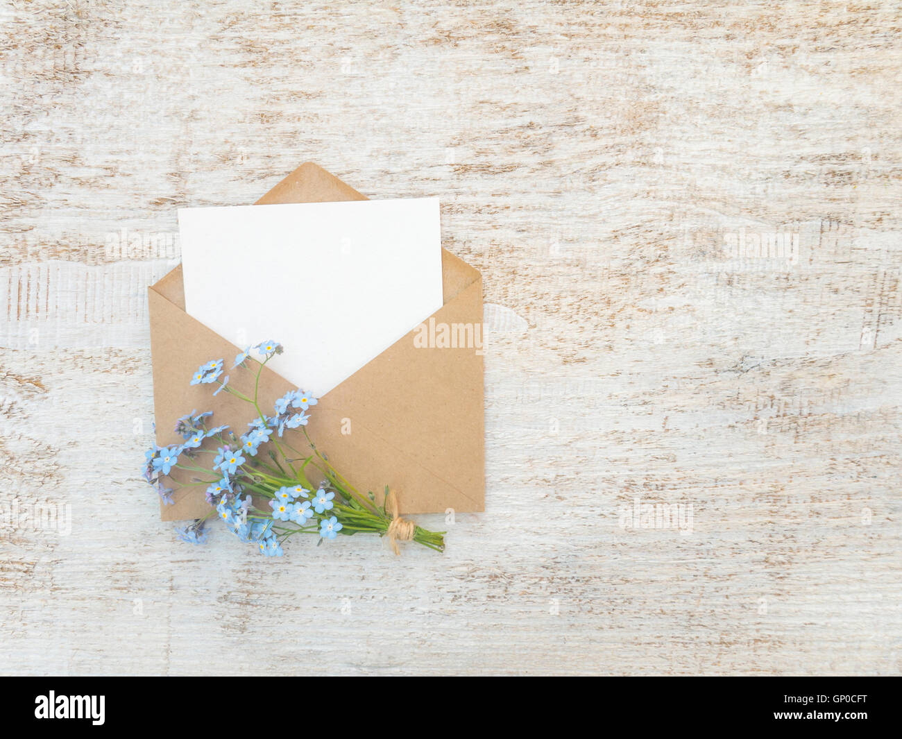 Carta marrone busta bianca con la scheda vuota e dimenticare blu-me-non bouquet di fiori legati con corda di iuta sul rustico di vernice bianca Foto Stock