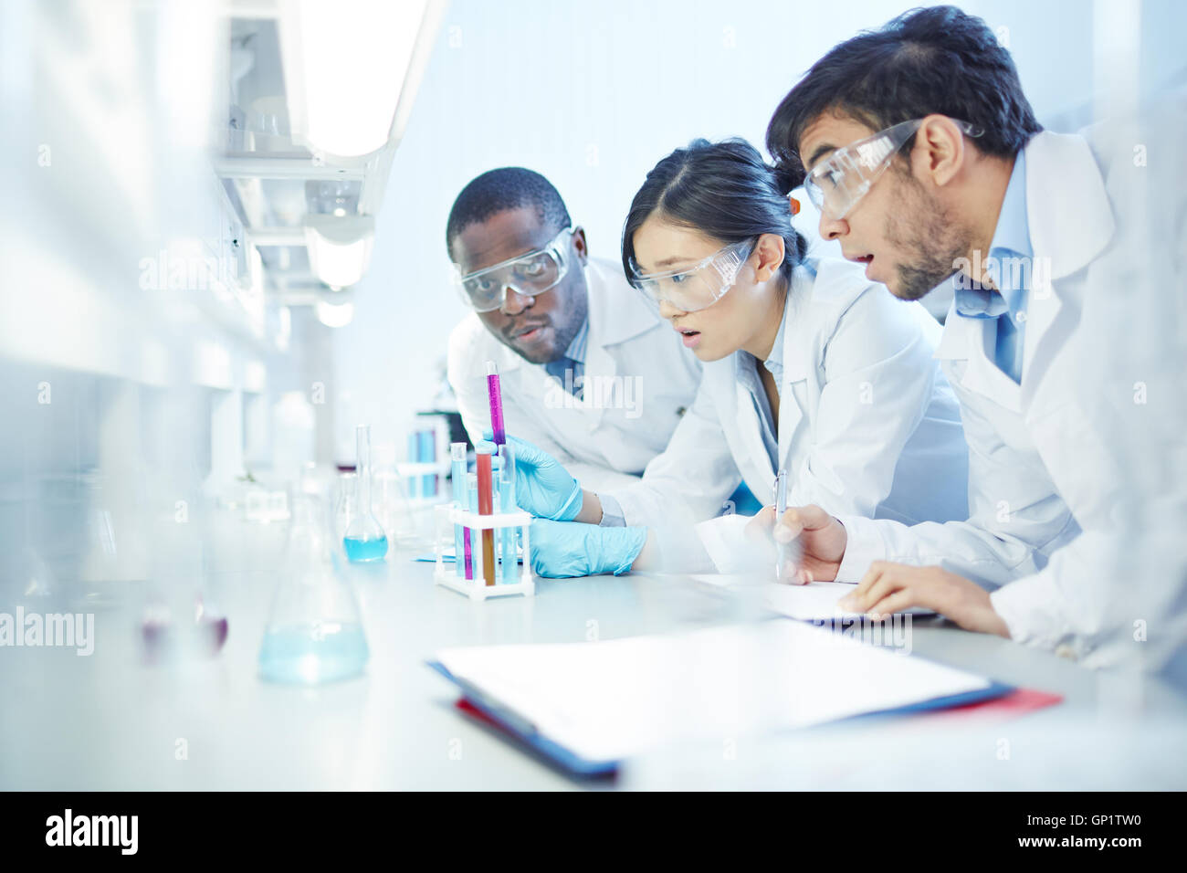 Sorpreso latino-americano maschio, maschio afro-americani e asiatici femmina gli scienziati del laboratorio in camice da laboratorio e occhiali di sicurezza a t Foto Stock