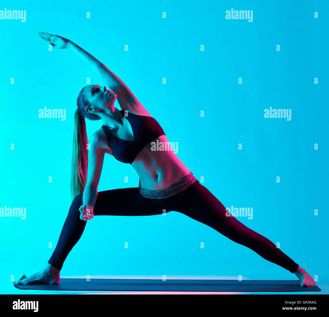 Una donna caucasica esercizio Utthita Parsvakonasana esercizi di yoga in silhouette studio isolato su sfondo blu Foto Stock