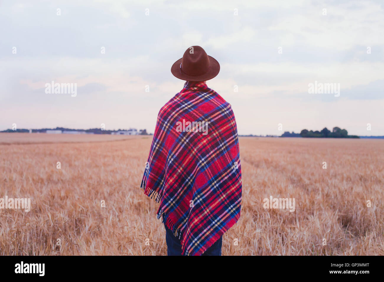 Vita rurale, lo stile di campagna, l'uomo in hat coperti in accogliente plaid a scacchi in piedi nel campo Foto Stock