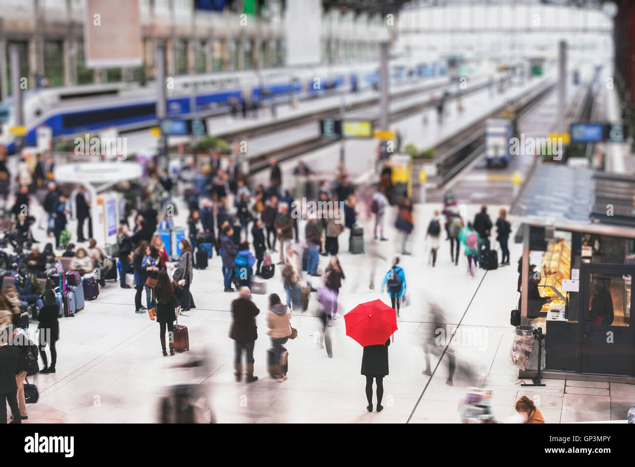 Donna con ombrello rosso in attesa alla stazione ferroviaria e sfocata persone in movimento, solitudine concept Foto Stock