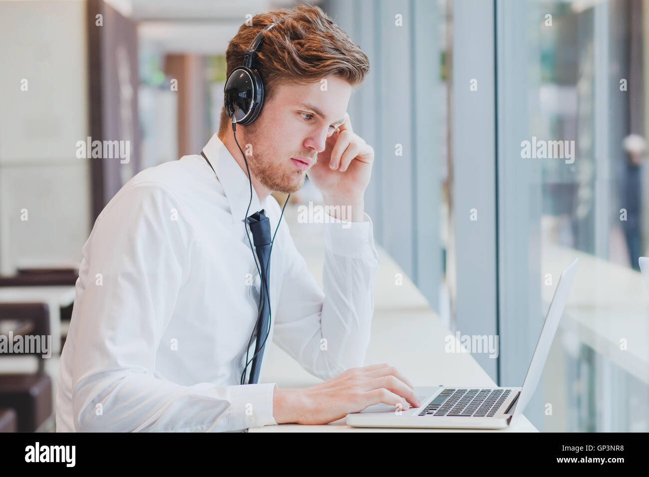 Imprenditore nel lavoro delle cuffie con il computer portatile in una moderna caffetteria interno Foto Stock