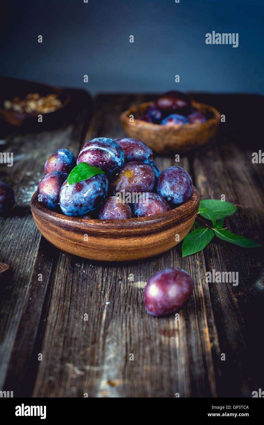 Fresco di prugne viola nella ciotola sul tavolo di legno. In verticale Foto Stock