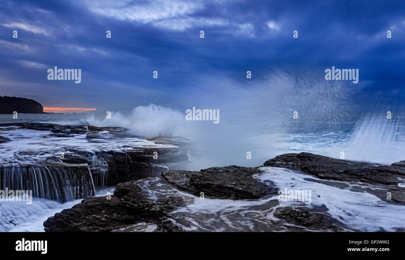 Forte splash di avvicinamento delle onde oceaniche erodendo le rocce di arenaria di Australia Pacific shore vicino a Sydney. Stormy sunrise meteo Foto Stock