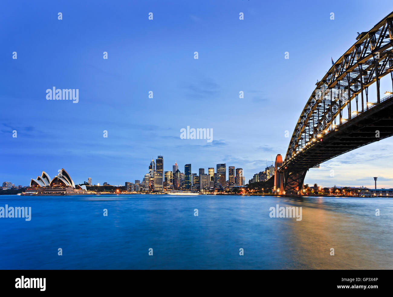 Lungomare della città di Sydney CBD intorno al Circular Quay con Harbour Bridge come si vede attraverso sfocata acque blu del porto al tramonto. Foto Stock