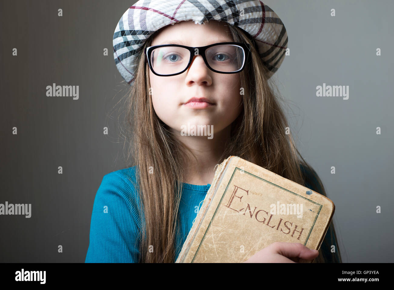 Grave la ragazza di occhiali e cappello a scacchi con libro inglese in mani Foto Stock