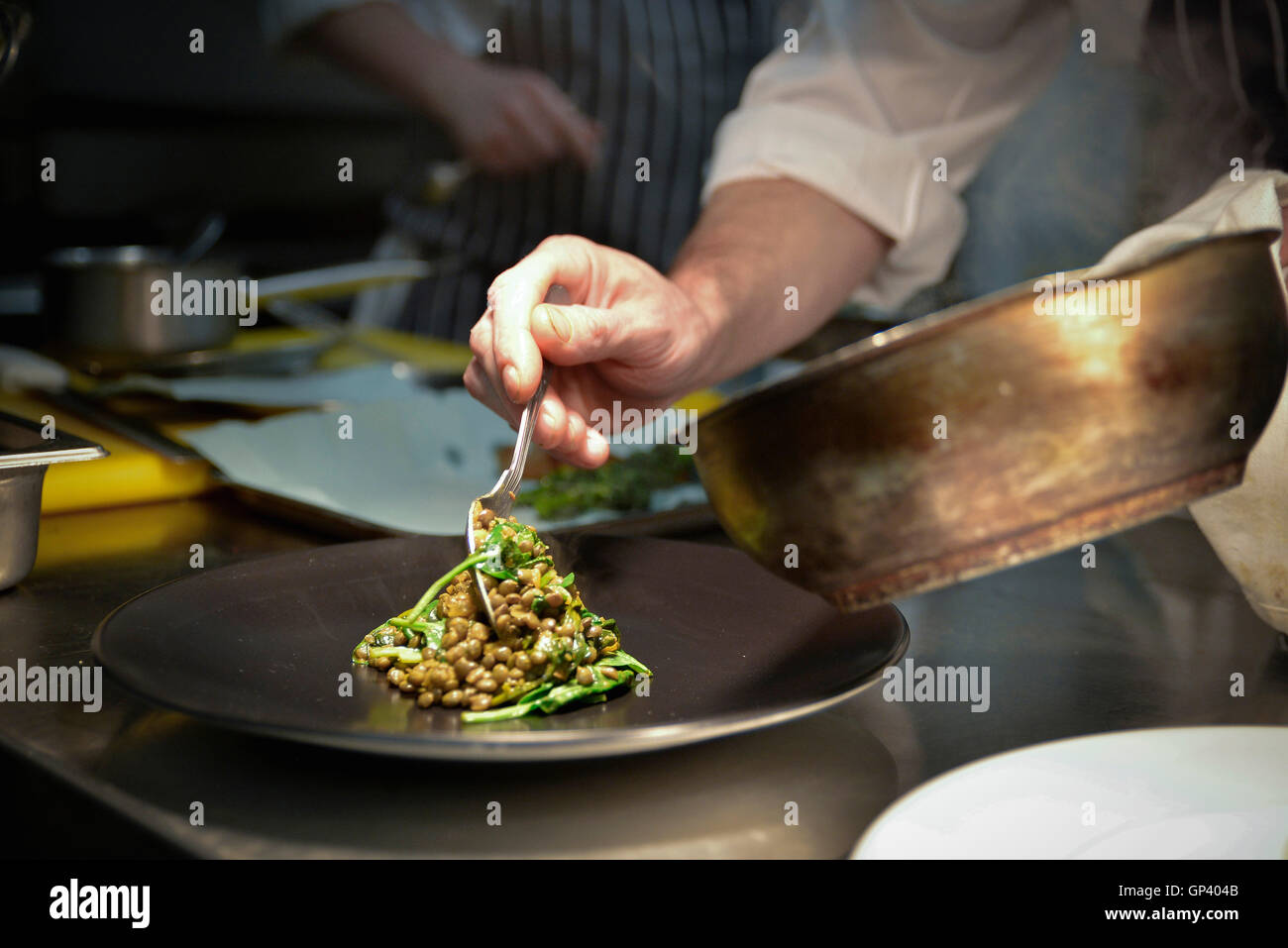 Lo Chef spooning piatto di lenticchie sul piatto di portata Foto Stock