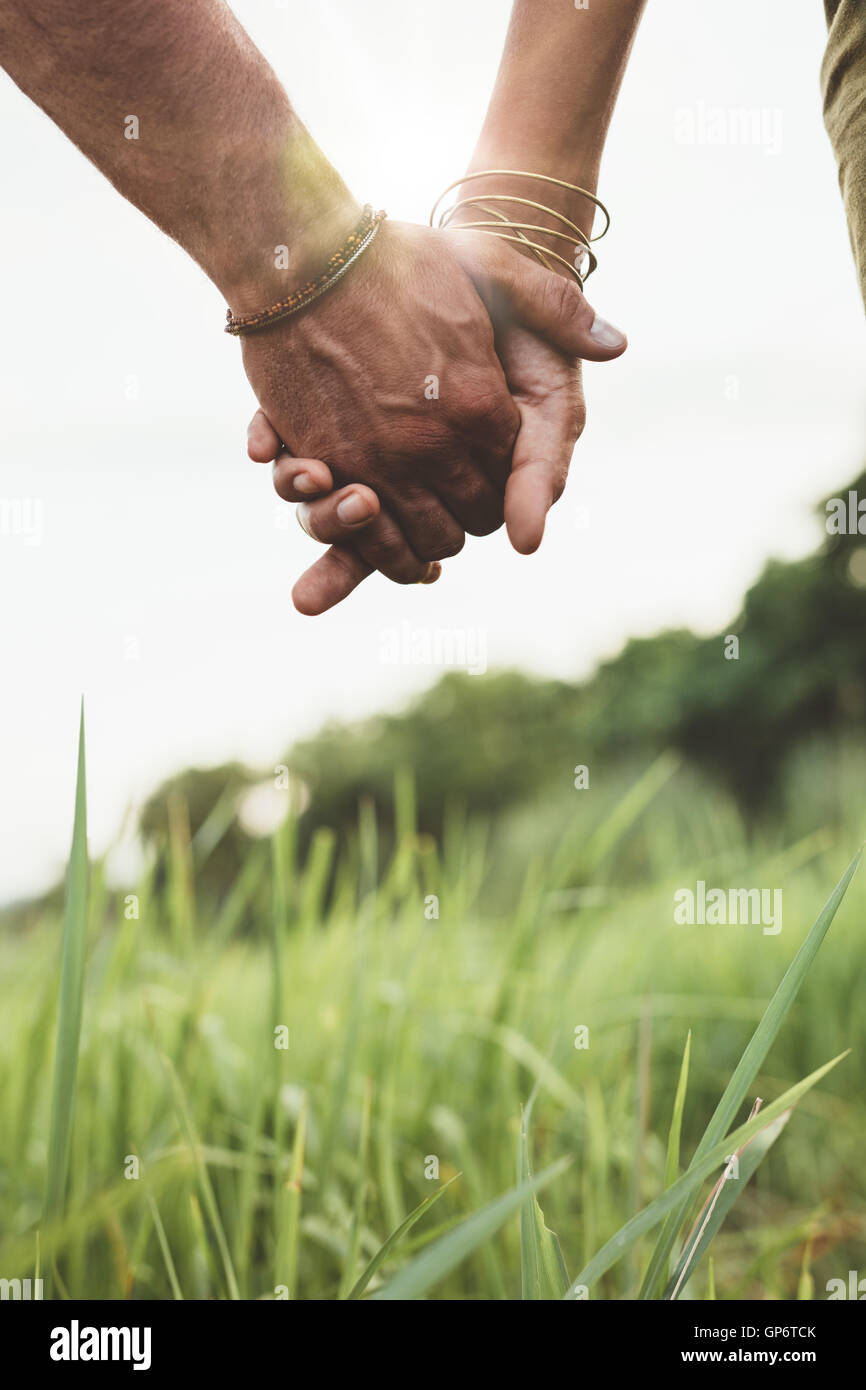 Colpo verticale di coppia giovane passeggiate attraverso prati mano nella mano con sun flare. Immagine ravvicinata con focus sulle mani dell uomo e w Foto Stock