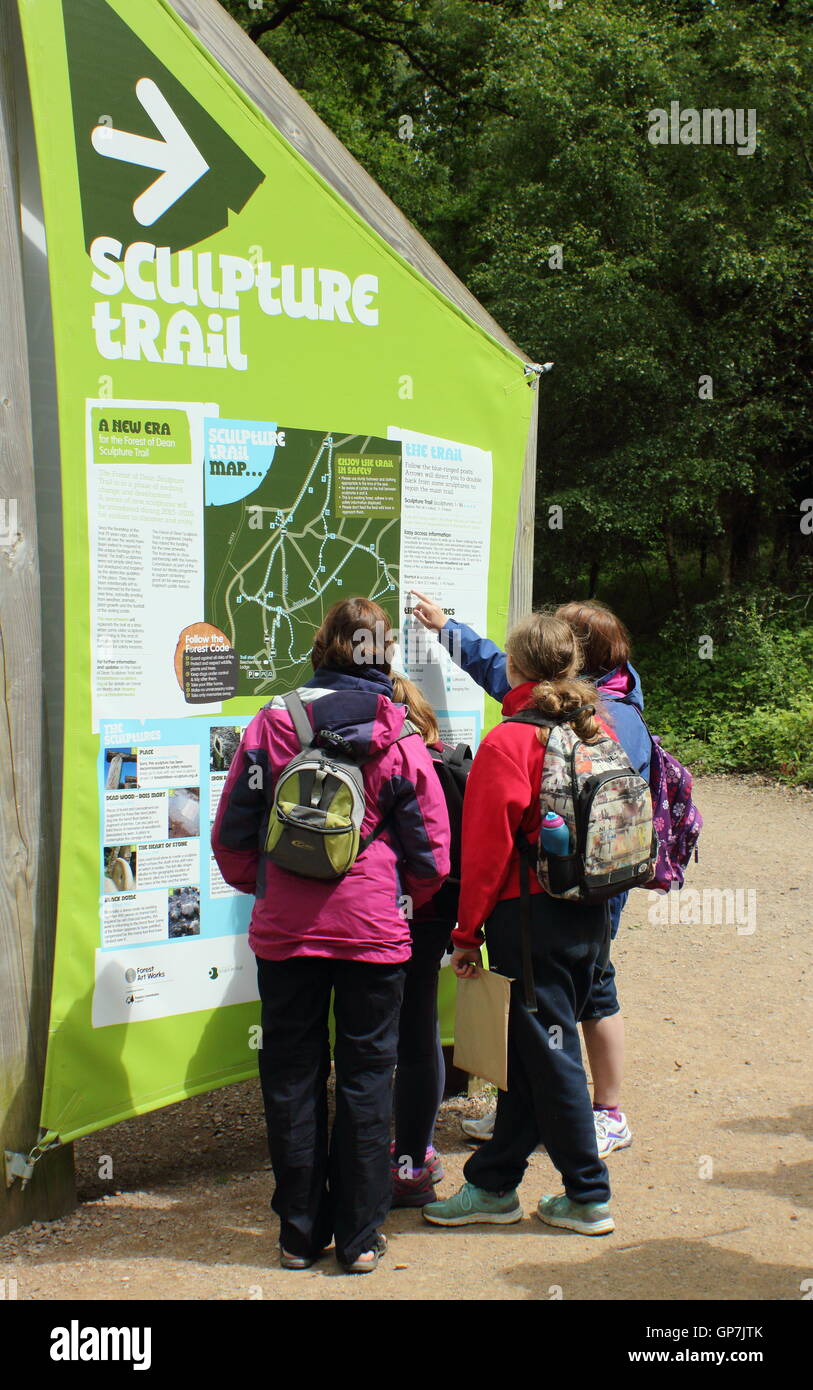 Visitatori check out information board all inizio del sentiero delle sculture nella Foresta di Dean, Beechenhurst, Gloucesterhire Foto Stock