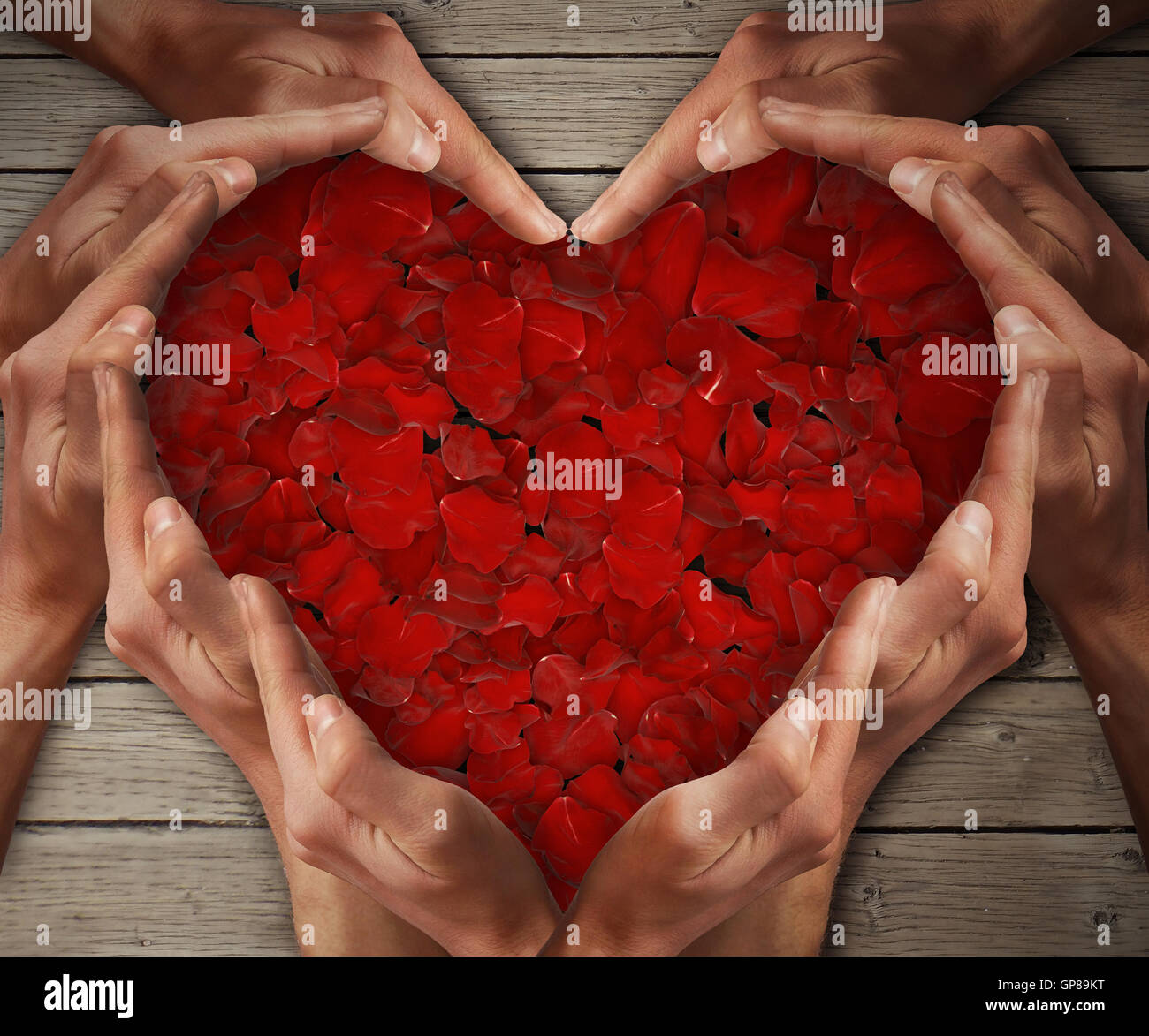 L'uomo le mani disposte a forma di cuore, con petali di rosa al centro su un tavolo di legno. Il concetto di amore Foto Stock