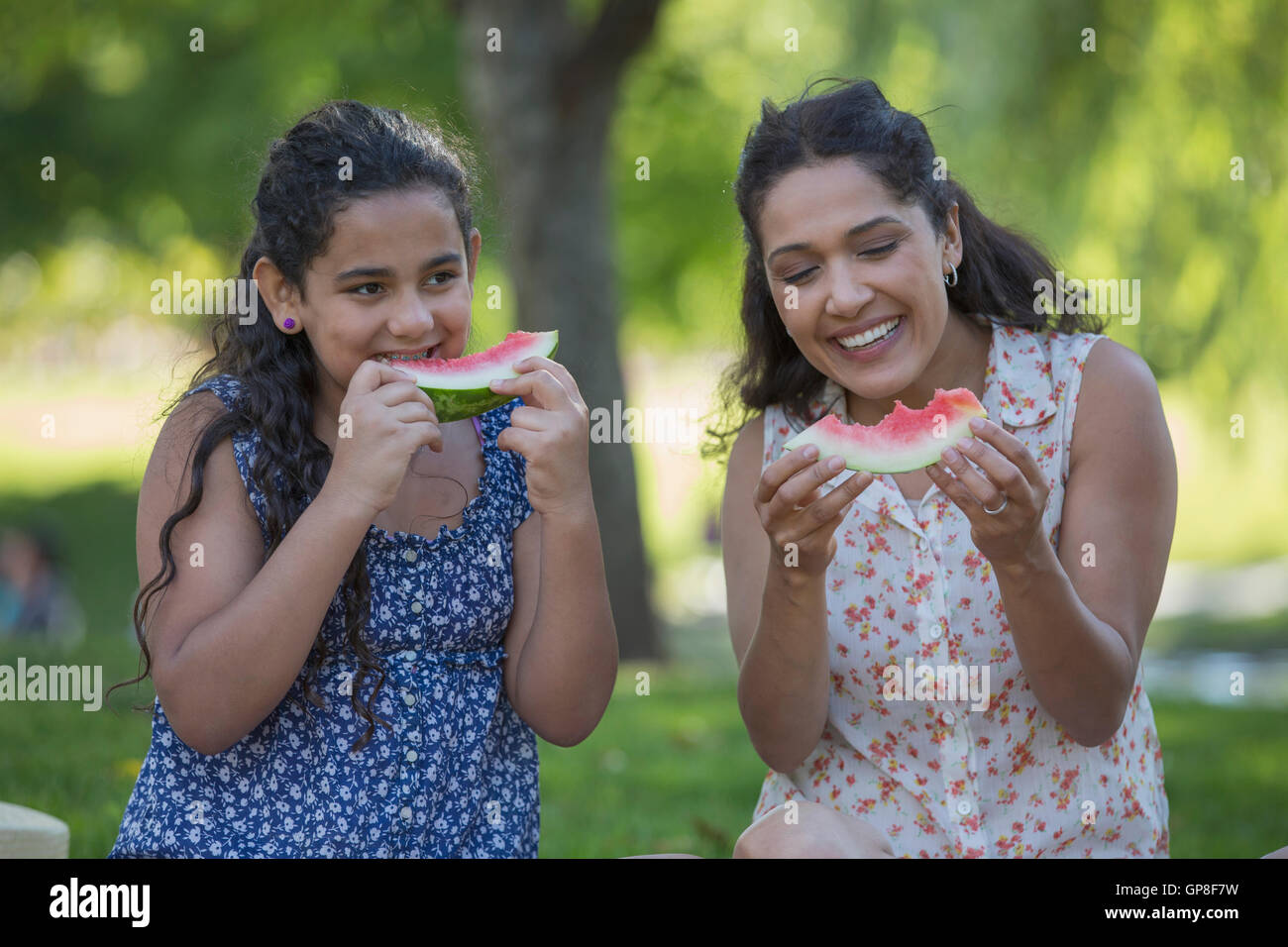 Felice madre ispanica con sua figlia teenager mangiando anguria in posizione di parcheggio Foto Stock
