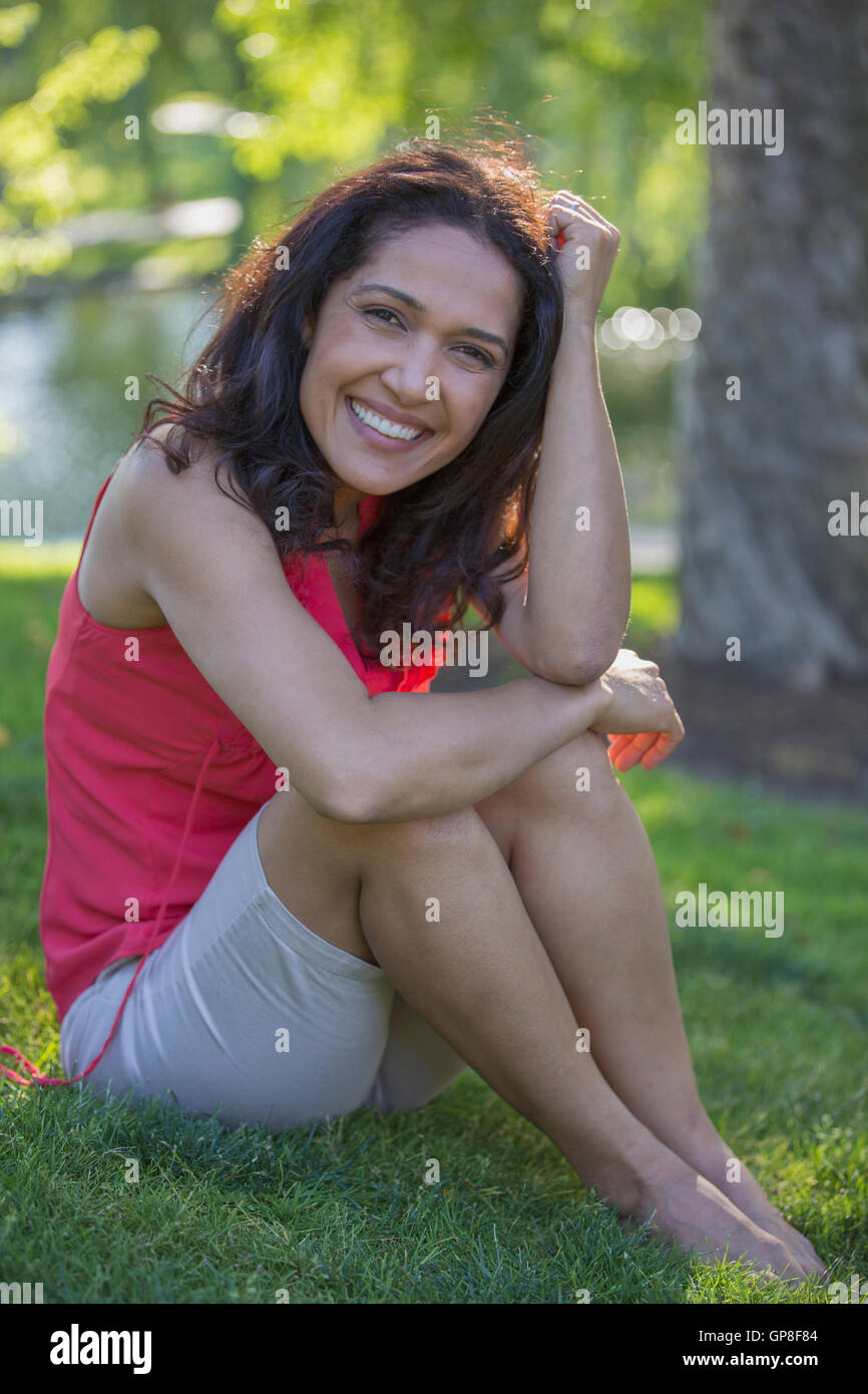 Ritratto di felice ispanico donna seduta in un parco Foto Stock