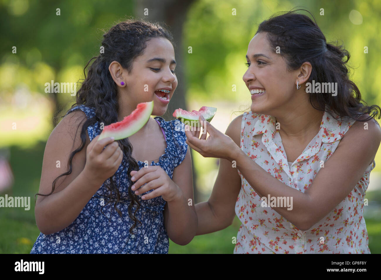 Felice madre ispanica con sua figlia teenager mangiando anguria in posizione di parcheggio Foto Stock