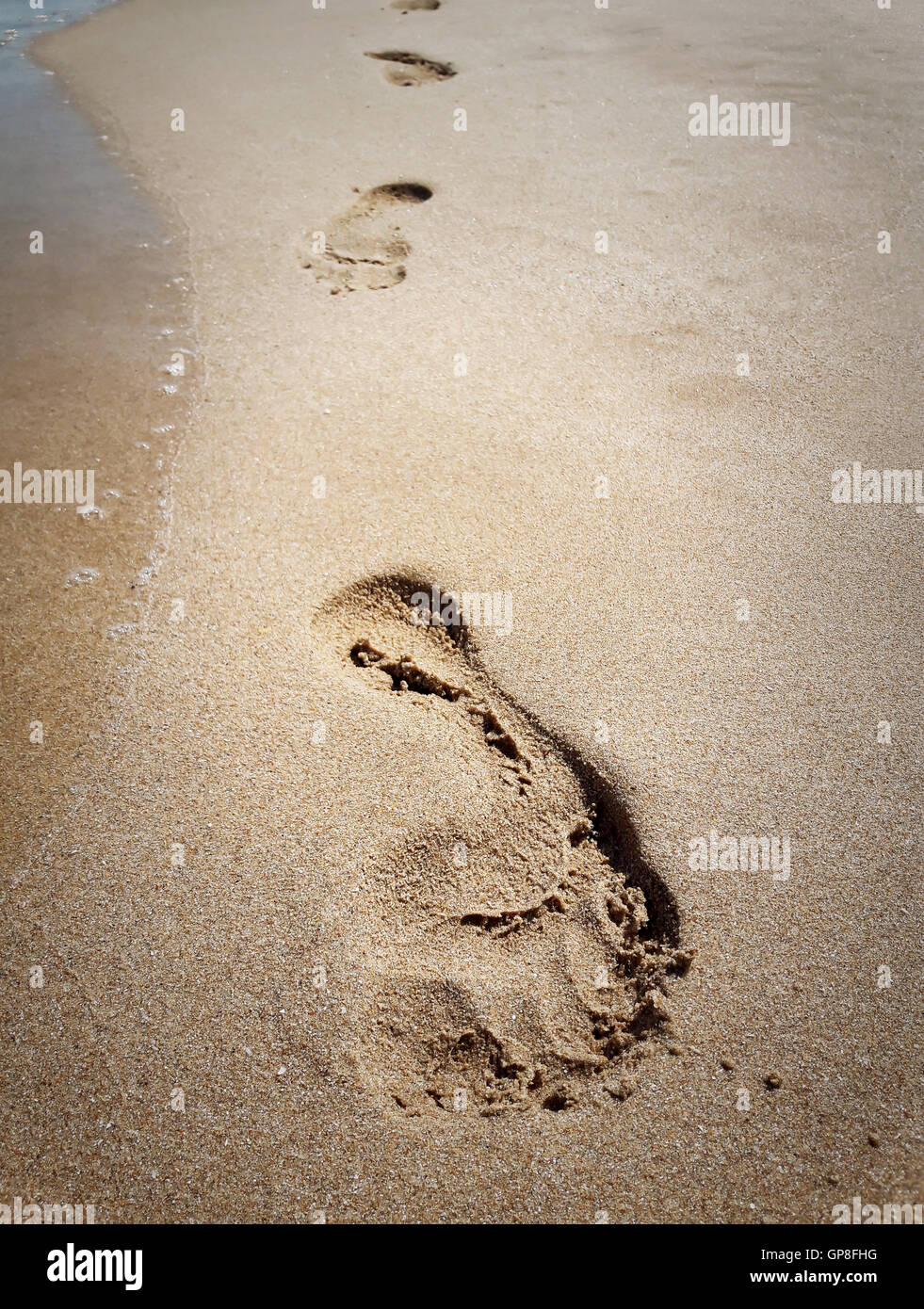 Primo piano di orme nella sabbia in spiaggia vicino all'acqua. Il concetto di viaggio Foto Stock