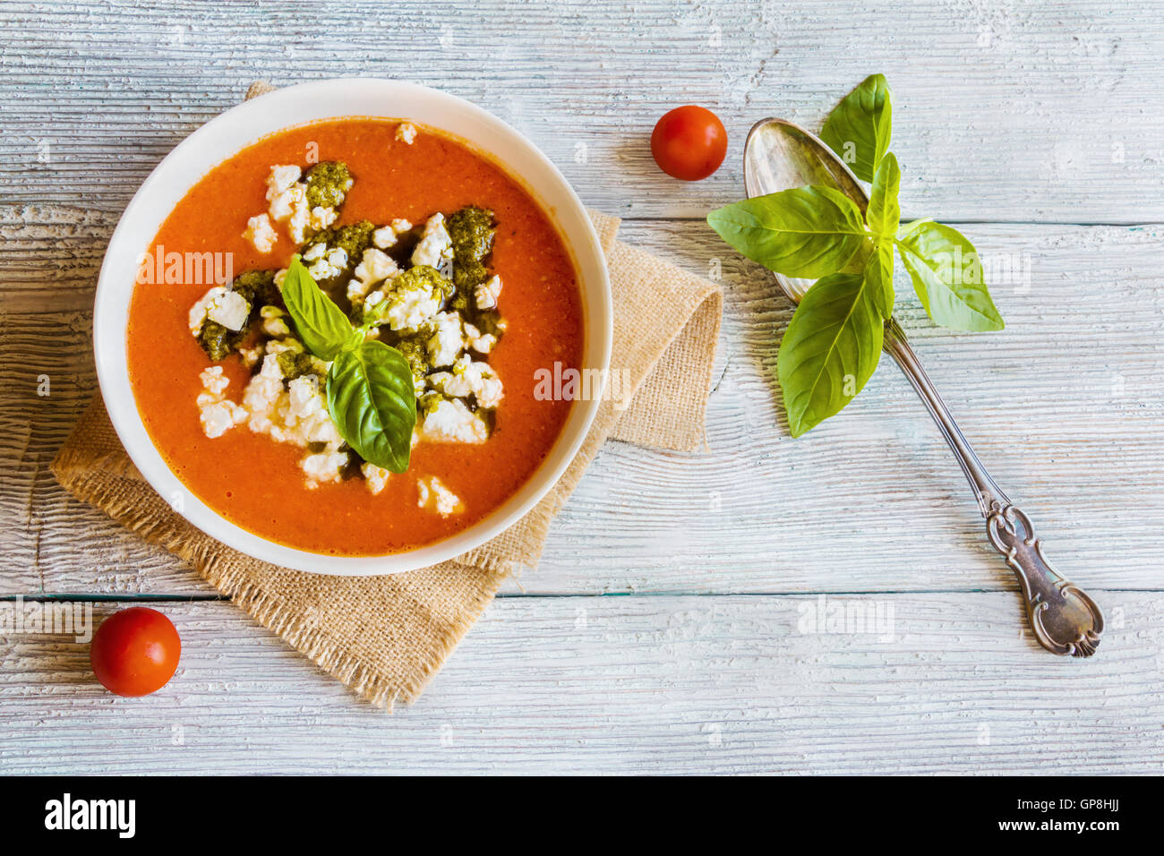 In casa vegetariano zuppa di pomodoro con il formaggio feta e pesto nella ciotola bianco su sfondo di legno. Servite con basilico fresco, Foto Stock