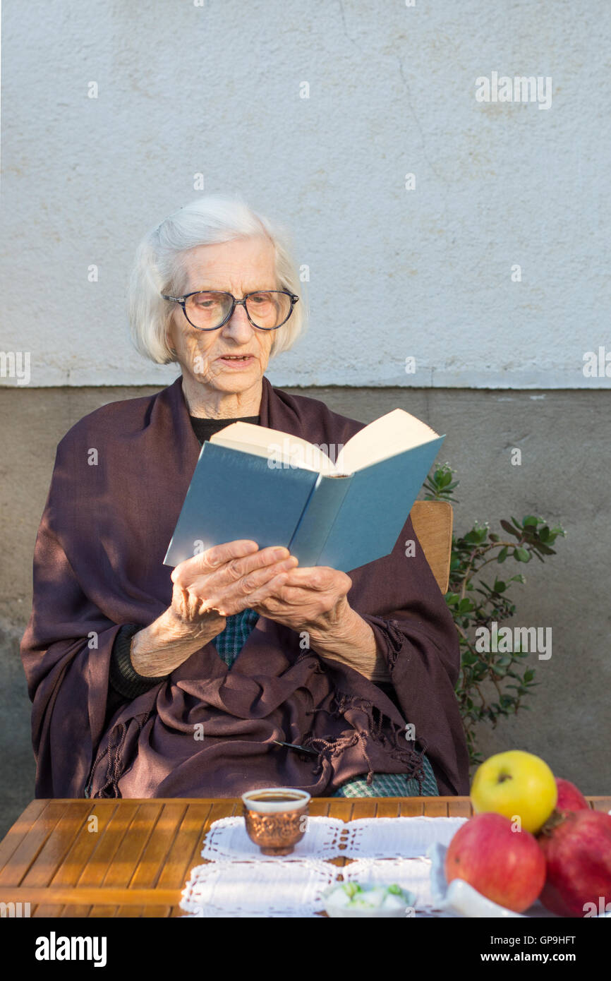 Senior donna la lettura di un libro blu all'aperto Foto Stock
