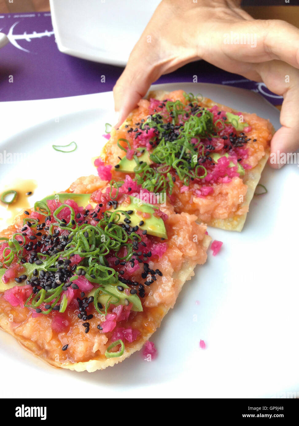 Giapponese cucina Messicana piatto - sashimi di salmone condito e decorate con avocado, di semi di sesamo tostati, anelli di cipolla su un taco Foto Stock