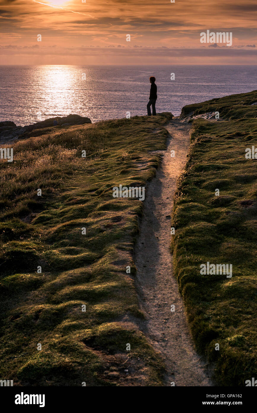 Una donna si erge su Porth Island che guarda al mare in un tramonto spettacolare. Foto Stock