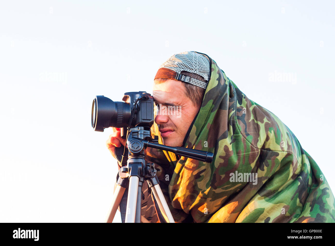 Primo piano di una mimetizzata paparazzi fotografo di scattare una foto con una fotocamera su un treppiede Foto Stock