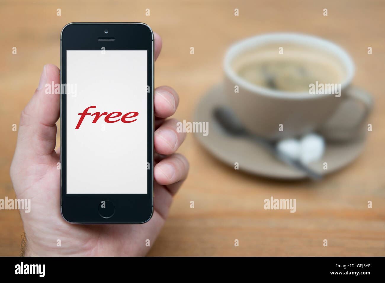 Un uomo guarda al suo iPhone che visualizza le telecomunicazioni libero logo operatore, con una tazza di caffè (solo uso editoriale). Foto Stock