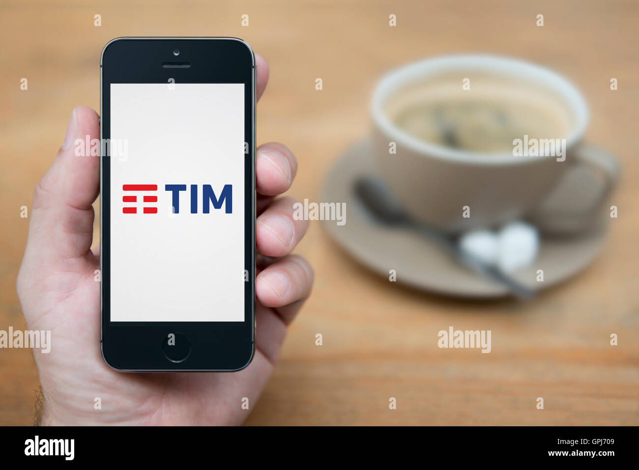 Un uomo guarda al suo iPhone che visualizza le telecomunicazioni TIM logo operatore, con una tazza di caffè (solo uso editoriale). Foto Stock