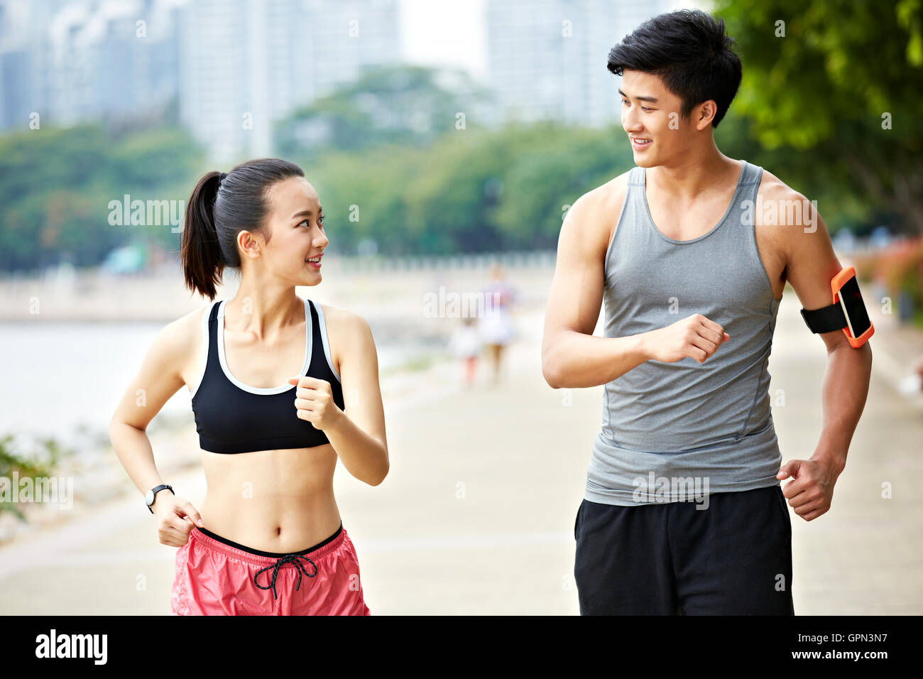 Giovane uomo asiatico e la donna giovane in esecuzione a fare jogging nel parco, guardando ogni altra conversazione Foto Stock
