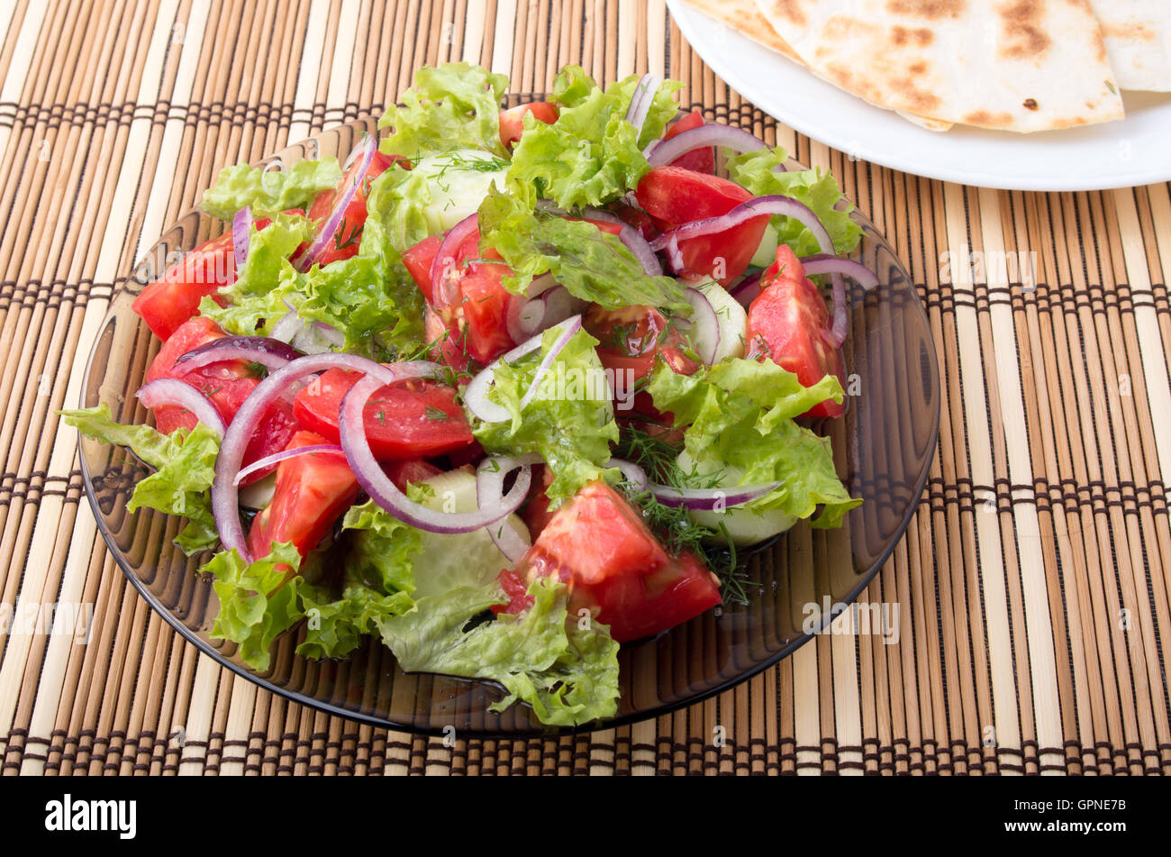 Close-up il piatto con una insalata di pomodoro a fette tagliate a fette, lattuga e cipolla in un marrone tappetino di bambù Foto Stock