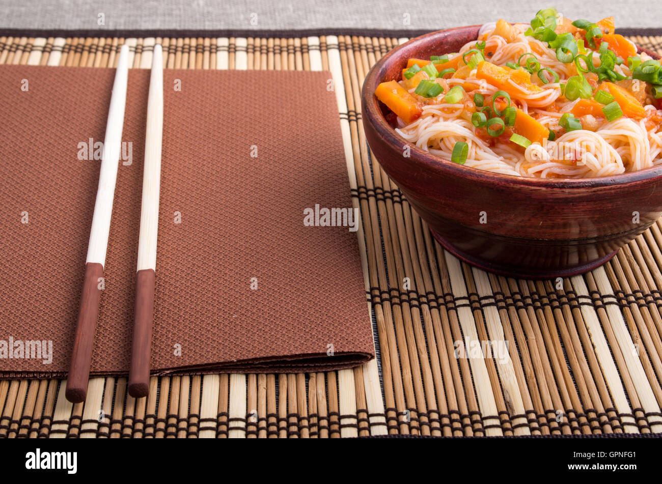 Vermicelli di riso hu-tue verdure con salsa di carote in un piccolo marrone ciotola di legno su un tappetino con striping vicino a bacchette Foto Stock