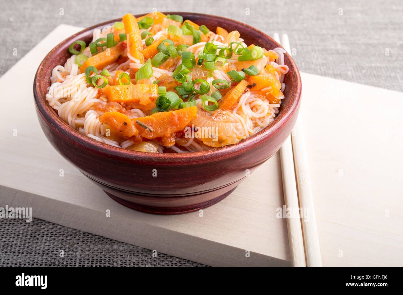 Primo piano cucina asiatica di riso tagliatelle e ragù vegetale in un piccolo marrone ciotola di legno su un supporto in legno Foto Stock