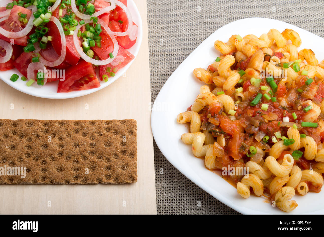 Vista dall'alto sui cavatappi la pasta con la salsa di legumi stufati servito con insalata di pomodoro crudo e segale cracker sul tessile indietro Foto Stock
