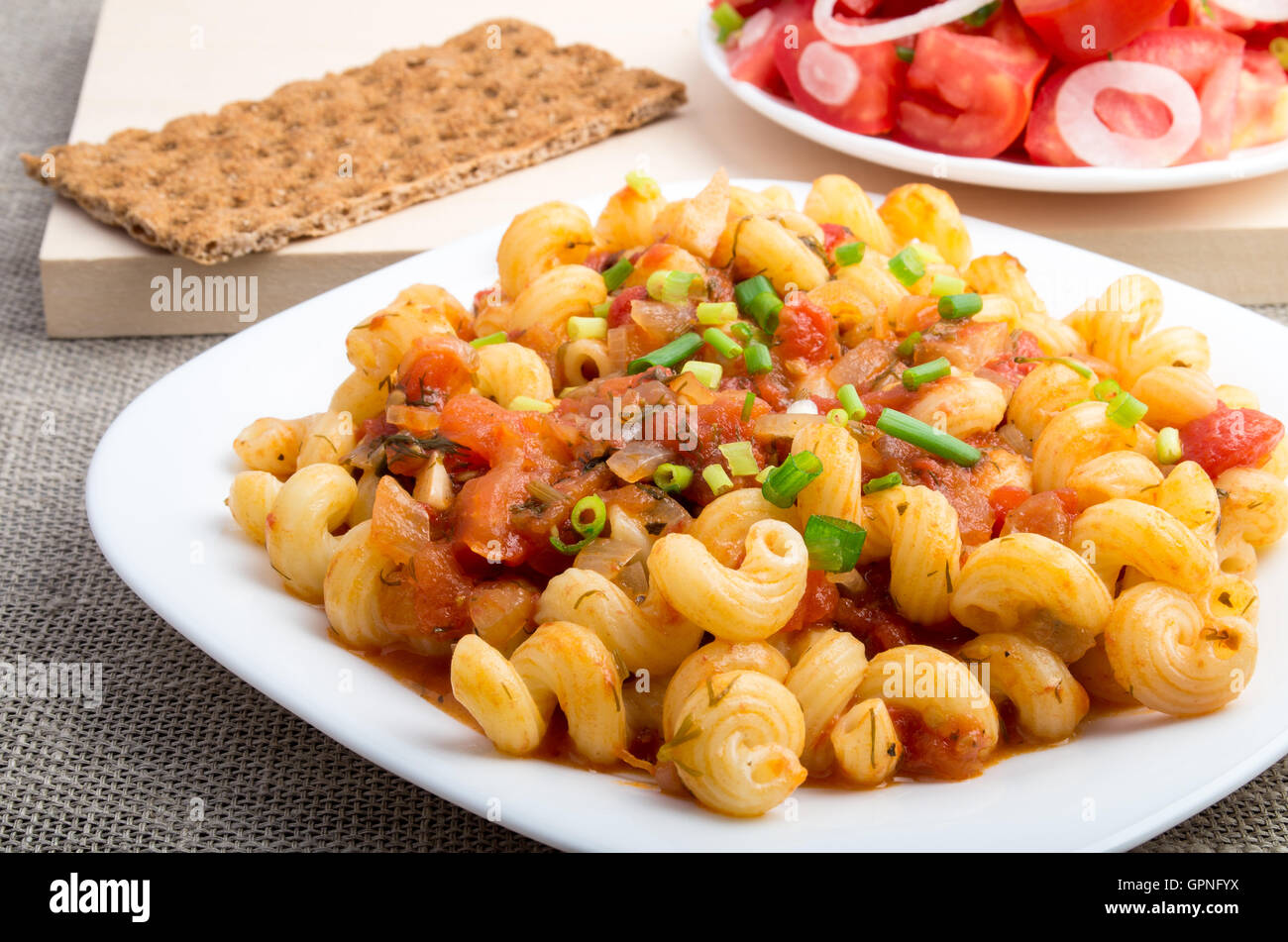 La pasta cotta cavatappi con legumi stufati e salsa di porri servito con insalata di pomodori e pane di segale sul tessile backgroun Foto Stock