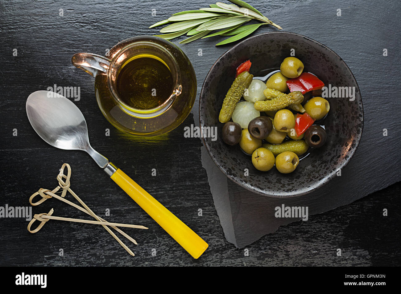 Ancora la vita di olio e Tapas su sfondo nero con olio di oliva vergine, cucchiaio e bastoncini swizzle Foto Stock