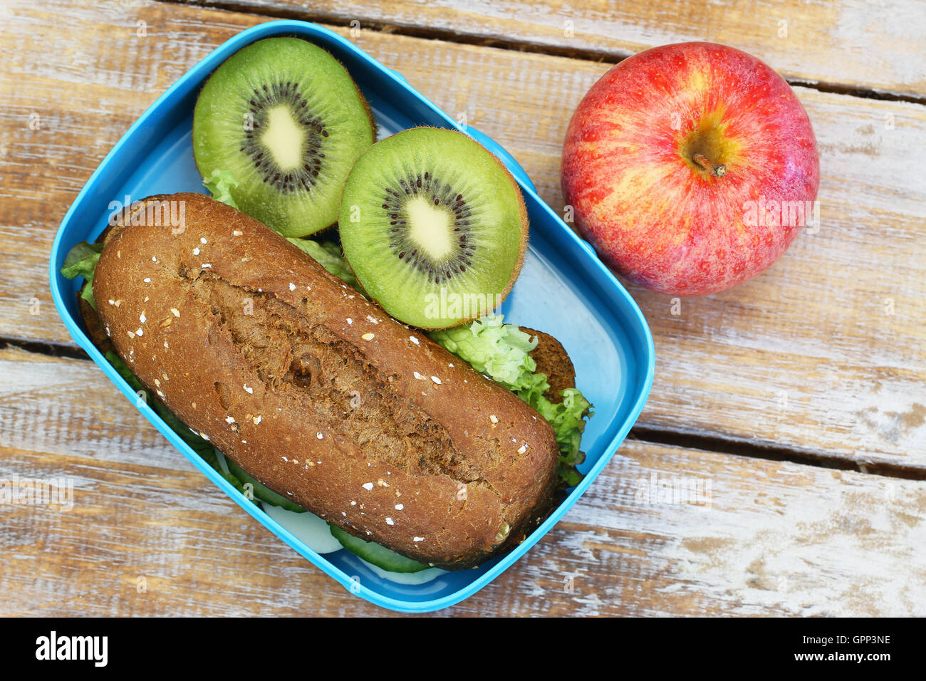 Pranzo al sacco contenente marrone sandwich di pane, kiwi e apple su rustiche superficie in legno Foto Stock